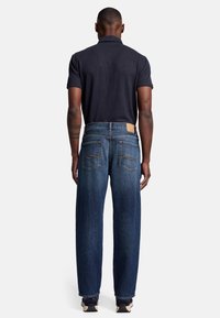 Granatowe dżinsy o prostym kroju, ze szczegó�łowymi tylnymi kieszeniami i beżową skórzaną naszywką na pasie, zestawione z granatowym polo.