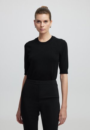 Top de punto negro de manga corta con cuello redondo, combinado con pantalones ajustados negros. Textura suave y diseño ajustado.