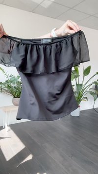 Sort off-shoulder top lavet af glat stof med en gennemsigtig flæseoverlag. Har en tætsiddende pasform og et label med teksten "ANNA FIELD."