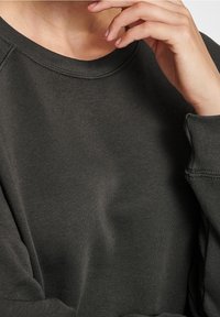 Felpa grigia scuro con colletto a girocollo, tessuto strutturato e vestibilità ampia. Dettagli di cucitura visibili lungo le cuciture e i polsini.