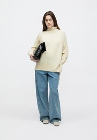 Kreminės spalvos didelio dydžio megztinis su aukštu kaklu, derinamas su mėlynais plačiomis kojomis džinsais. Juoda delninė papildys aprangą.
