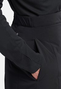 Zwarte gewatteerde rok met een gladde textuur en een brede tailleband. Beschikt over een zijzak en is gecombineerd met een nauwsluitend shirt met lange mouwen.