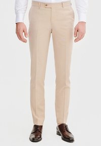 Beżowe spodnie garniturowe wykonane z lekkiego materiału, z prostą nogawką, przednimi kieszeniami i gładką fakturą. Brązowe buty eleganckie.