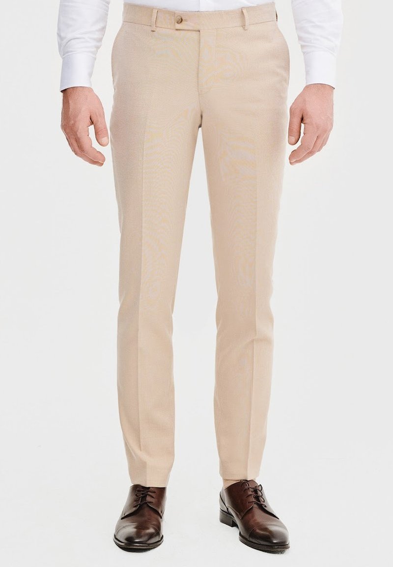 Beżowe spodnie garniturowe wykonane z lekkiego materiału, z prostą nogawką, przednimi kieszeniami i gładką fakturą. Brązowe buty eleganckie.