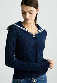 Cardigan lavorato a maglia blu navy con colletto da marinaio a righe bianche, motivo testurizzato e bottoni rotondi lungo la parte anteriore.