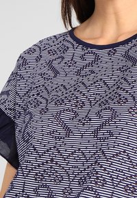 Granatowa i biała koszulka w paski z kwiecistym wzorem, z okrągłym dekoltem i krótkimi rękawami, zdobiona cekinami dla dodatkowego efektu.