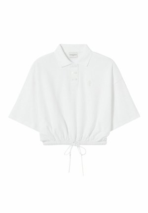 Polo blanc raccourci avec une patte de boutonnage, manches courtes, ourlet à cordon de serrage et broderie de logo discrète sur la poitrine. Texture de tissu doux.