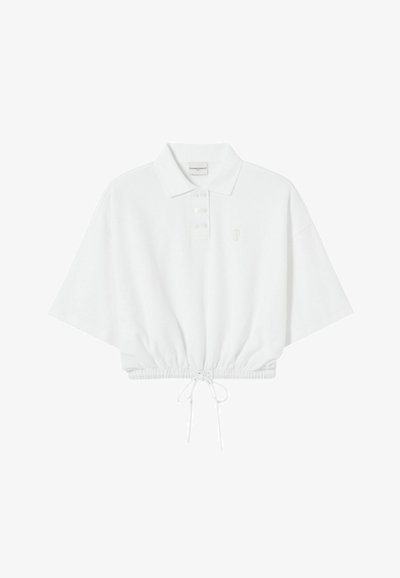 Polo blanc raccourci avec une patte de boutonnage, manches courtes, ourlet à cordon de serrage et broderie de logo discrète sur la poitrine. Texture de tissu doux.