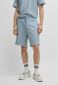 Shorts en coton bleu clair avec une taille élastique et un cordon de serrage, associés à un t-shirt assorti et des baskets grises avec des chaussettes blanches.