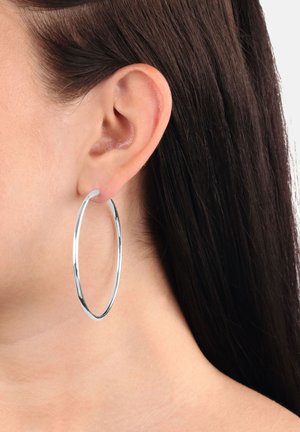 Primer plano de la oreja de una mujer con cabello largo y oscuro, que lleva un gran aro de plata delgada y brillante.