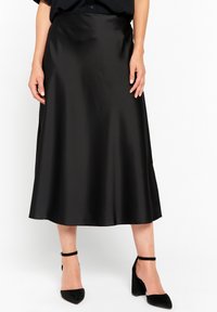 Gonna midi nera in satin a forma ad A con una texture liscia, caratterizzata da una vita alta. Abbinata a scarpe con tacco nere e a una maglietta ampia.
