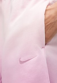 Χέρι που ακουμπά στην τσέπη των ανοιχτό ροζ σορτς Nike με κεντημένο το λογότυπο Nike swoosh σε μαλακό ύφασμα.