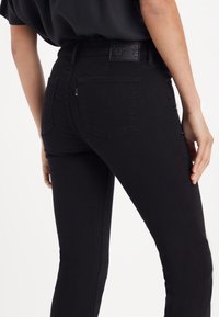 Jeans de mezclilla negros con un corte ajustado, que presentan un diseño texturizado en el bolsillo trasero y un parche de cuero con la marca en la cintura.