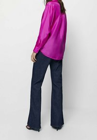 Fuchsia satijnen blouse met een hoge kraag en lange mouwen, gecombineerd met donkerblauwe uitlopende spijkerbroeken en zwarte schoenen met hoge hakken.