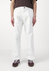 Witte katoenen broek met een rechte snit, voorzien van een knopsluiting aan de voorkant en zijzakken. Gecombineerd met bruine sneakers.