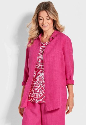 Chemise en lin rose avec des manches retroussées, fermeture à boutons, superposée à un haut blanc et rouge à motifs. Pantalon rose assorti avec une coupe ample.