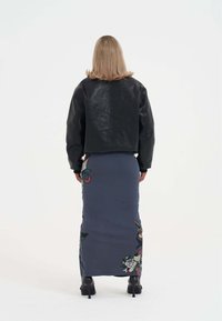 Černá kožená zkrácená bunda s embosovaným vzorem na zádech, kombinovaná s dlouhou tmavě modrou sukni s barevnými potiskovými vzory. Černé podpatky.