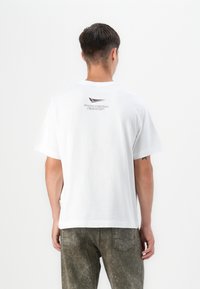 White cotton T-shirt featuring a crew neck, short sleeves, and a small printed logo in dark maroon on the upper back.