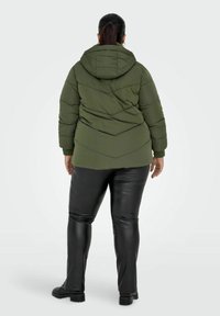 Veste rembourrée vert foncé avec capuche, dotée d'un motif de piquetage en chevrons, associée à un pantalon en similicuir noir et des chaussures plates noires.