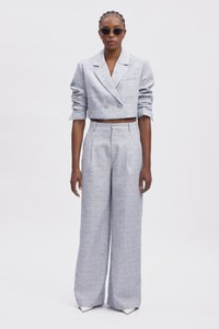 Blazer gris clair cintré avec deux boutons, associé à un pantalon large taille haute. Le modèle porte des lunettes de soleil noires. Texture lisse.