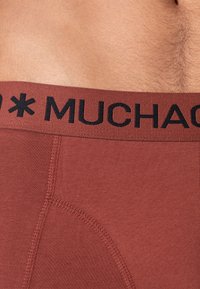Bruna boxershorts med en svart elastisk midjeband med texten "MUCHACHO", har mjukt tyg, en tät passform och förstärkta sömmar.