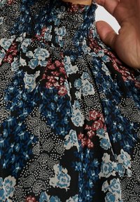 Černé květinové šaty s nabíraným výstřihem, modrými a červenými květinovými vzory a složitými paisley detaily na lehkém materiálu.