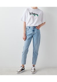 Valkoinen t-paita, jossa on vihreä ja musta "Woman" -kirjonta, vaaleansiniset korkeavyötäröiset farkut ja musta-valkoiset tennarit. Rentoa asua.