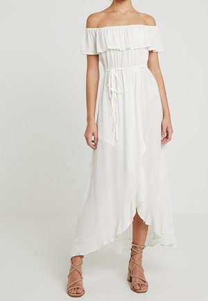 Vestido blanco sin hombros con escote de volantes, cintura ceñida con lazo, dobladillo asimétrico, combinado con sandalias marrones de tacón bloque con cordones.