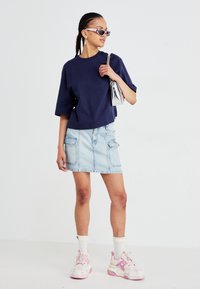 Marineblå cropped t-shirt, lys blå denimnederdel med lommer, hvide crew-sokker, lyserøde sneakers med dekorative snørebånd og en sølvfarvet håndtaske.