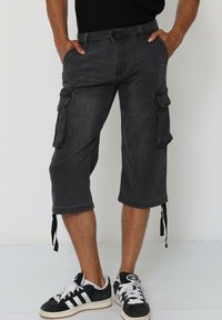 Shorts cargo en denim noir avec une coupe à longueur de genou, plusieurs poches latérales, ourlets avec cordon de serrage réglable et finition délavée.