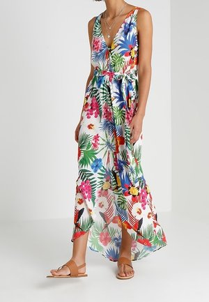 Robe maxi sans manches à col en V avec imprimé floral tropical, fente latérale, taille nouée, portée avec des colliers superposés et des sandales plates couleur beige.