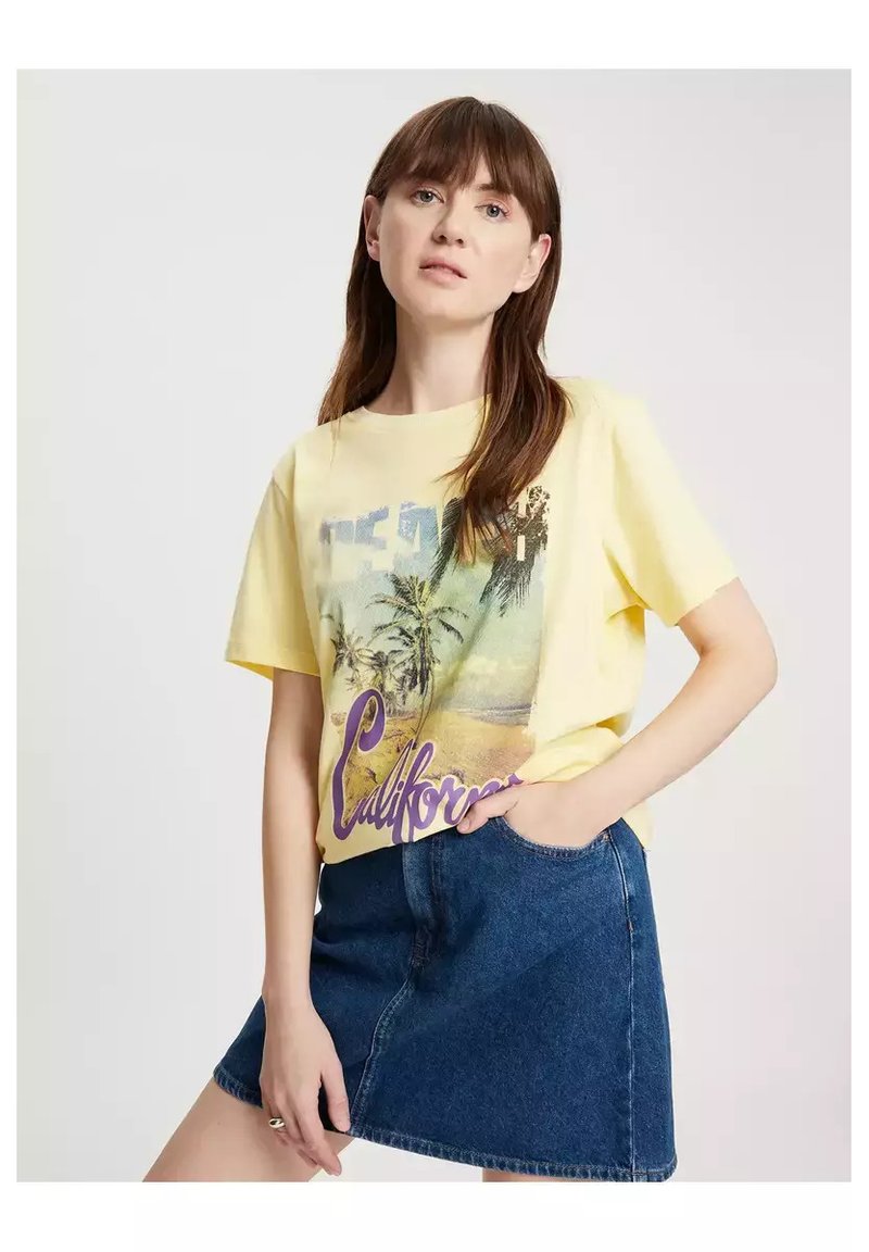Żółta koszulka z krótkim rękawem z grafiką palmy i napisem "California" w kolorze purpurowym, połączona z dżinsową spódnicą w kształcie litery A.