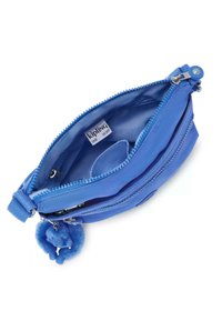 Federa blu con zip realizzata in tessuto testurizzato, con doppi scomparti e un charm a pompon blu morbido attaccato. L'etichetta interna riporta "Kipling Live Light."