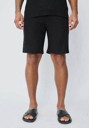 Shorts en lin noirs avec une taille élastique, coupe droite et un fit décontracté. Portés avec des sandales noires minimalistes.