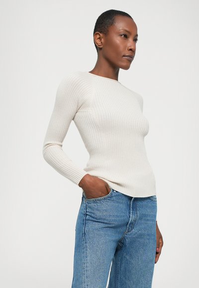 Cream ribbed long-sleeve sweater with a round neck, paired with light blue denim jeans. Smooth texture, fitted design, and casual style.