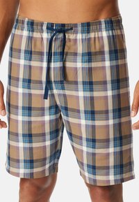 Shorts à carreaux en brun, bleu et blanc avec une taille élastique et un cordon de serrage. Présente différentes tailles de carreaux et une texture de tissu lisse.