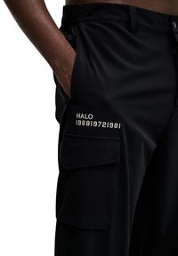 Svarta cargobyxor med en slät textur, med sidofickor och broderad "HALO 196819721981" detalj på låret.