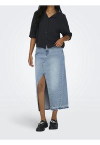 Dark button-up shirt, light denim maxi skirt with front slit, featuring frayed hem and a relaxed fit, paired with black loafers.