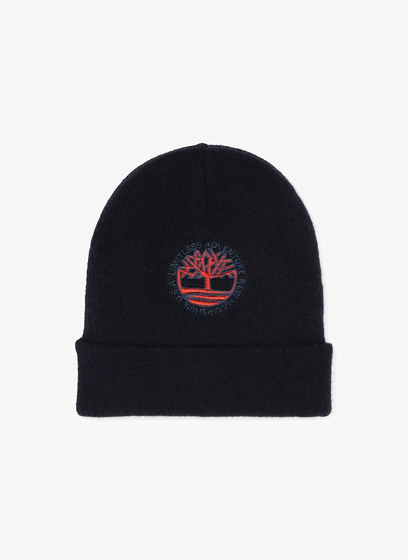 Gebreide beanie in donker marineblauw met een omgeslagen rand. Kenmerkt zich door een cirkelvormig, geborduurd boomlogo met rode en blauwe tekst rondom het ontwerp.