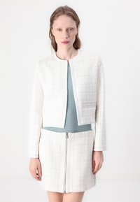 Valge tweed jakk ümara kaelusega, lühendatud disainiga ja kahe esipocketiga, koos sinise ribaga topi ja sobiva valge seelikuga, millel on lukku.