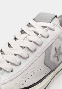 Gray and white sneaker made of canvas and suede with thick laces, perforated detailing, star logo, and a contrasting black sole.