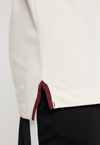 Biała bawełniana koszulka z bocznym rozcięciem z bordowym akcentem. Teksturowana tkanina o prostym kroju, zestawiona z czarnymi spodniami.