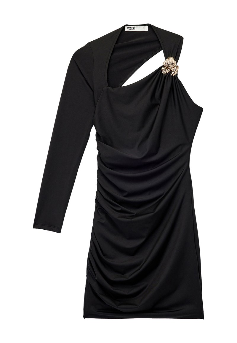 Sort langærmet kjole med rynket tekstur, asymmetrisk udskæring og en dekorativ blomsterbrosche på den ene skulder.