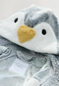 Zacht grijs en witte pluizige hooded nachtmode met pinguïn gezicht en gele snavel op de kap, met het label "Nachtmode van Next."