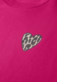 Tissu rose vif avec une petite pièce en forme de cœur présentant un motif léopard gris et beige près du col.