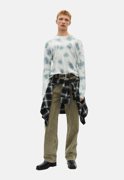 Maglietta a maniche lunghe tie-dye in blu e bianco, abbinata a pantaloni verde oliva. Camicia nera a scacchi legata in vita. Stivali neri completano il look.