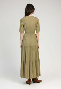 Robe longue de couleur vert olive avec un design à volants, des manches courtes bouffantes et une taille cintrée. Le tissu semble doux avec une finition texturée.