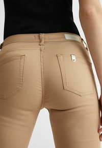 Jeans beige aderenti in tessuto morbido, con vita media, due tasche posteriori e un piccolo etichetta con logo sopra la tasca destra.