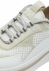 Sneaker con una parte superiore beige e bianca testurizzata, caratterizzata da un motivo a maglia, strisce grigie di accento e una suola bianca spessa.