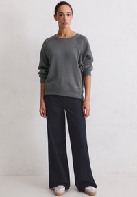 Szara bluza z okrągłym dekoltem, rękawami raglanowymi i ściągaczem na dole, zestawiona z granatowymi szerokimi spodniami i białymi sneakersami z beżowymi podeszwami.